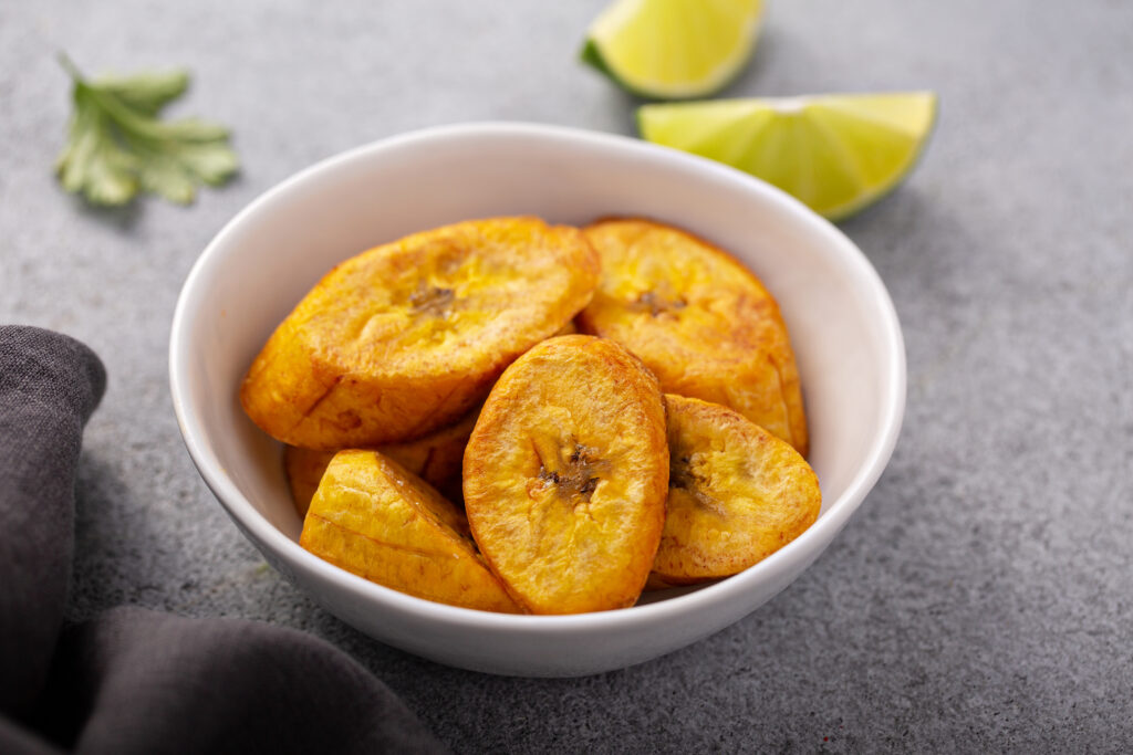 Fried plantain in a white bowl with lemon and greens