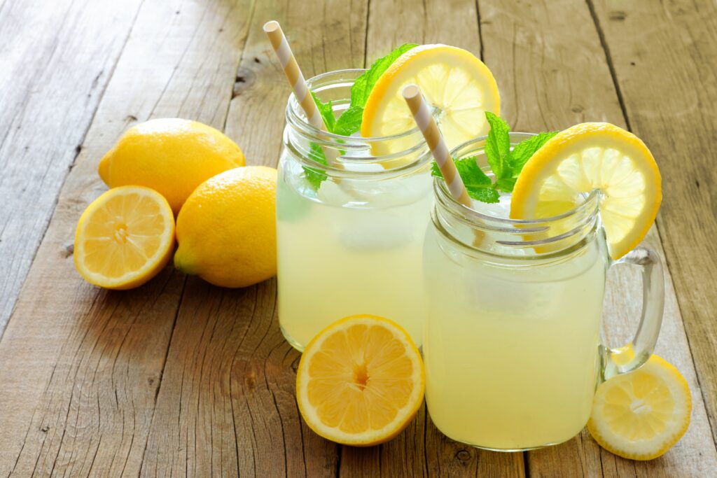 "refreshing lemonade with ice, lemon slice and mint sprig in glass on wooden table"