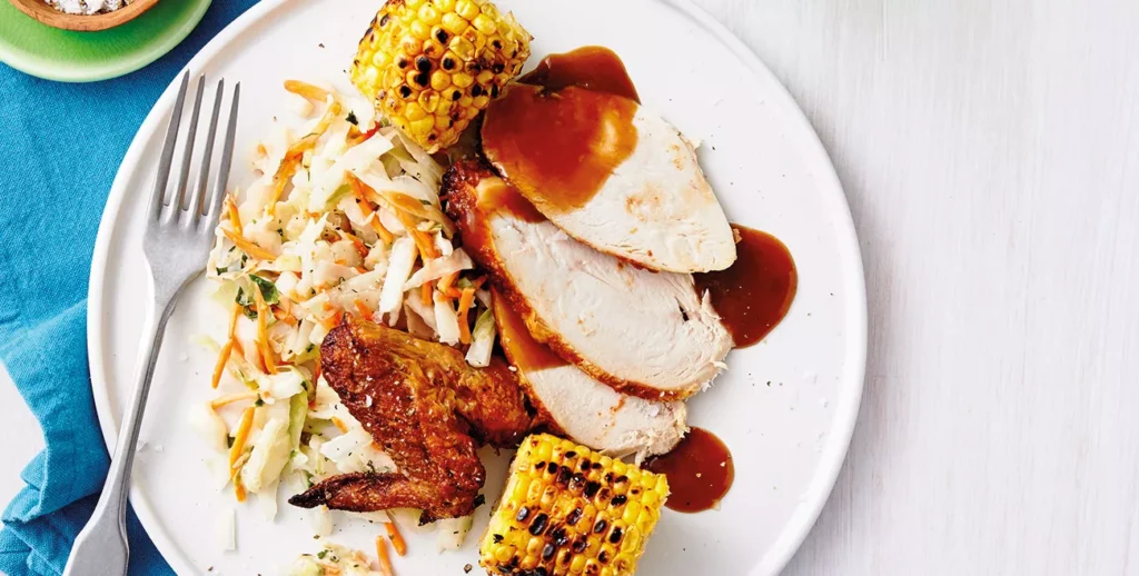 "Cooked chicken with gravy with cut pieces of chicken breast, coleslaw and corn"