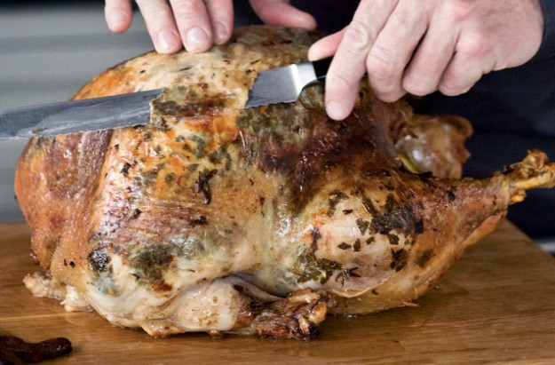 "A cooked whole chicken with lots of herbs and butter under the skin being carved by a chef"