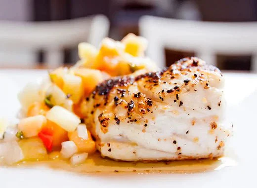 "A piece of pan seared grouper with a light sauce and vegetables in the backgroun
