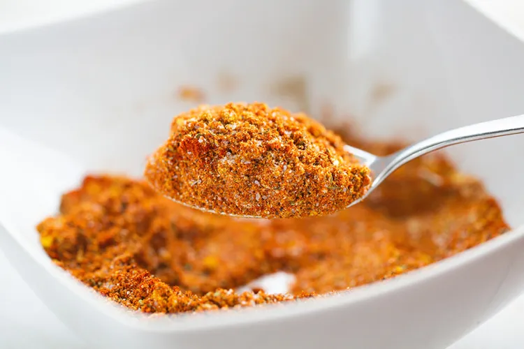 "Orangey hue dry spice rup in a white bowl with a heaping spoonful taken up and the rest in a white bowl"