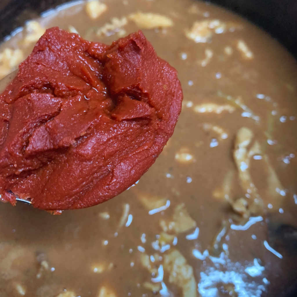 "Conch stew adding tomato paste to conch stew pot"