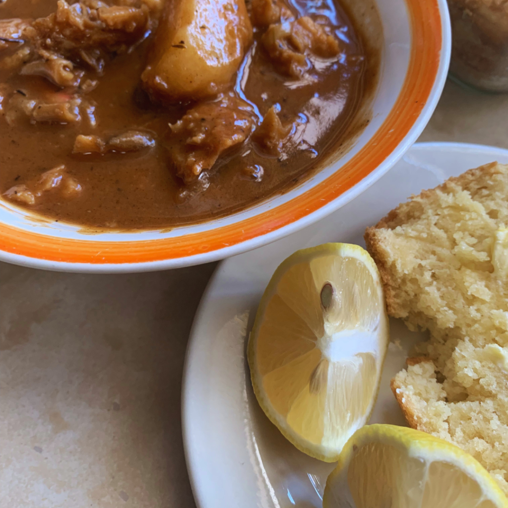 "Conch Stew with Johnny cake and lemon wedges on a white plate and orange and white bowl"