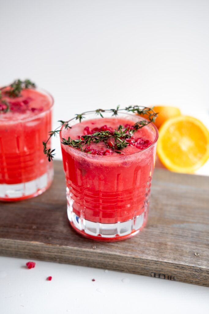 "Cranberry cocktail on wooden base with orange cut in half"
