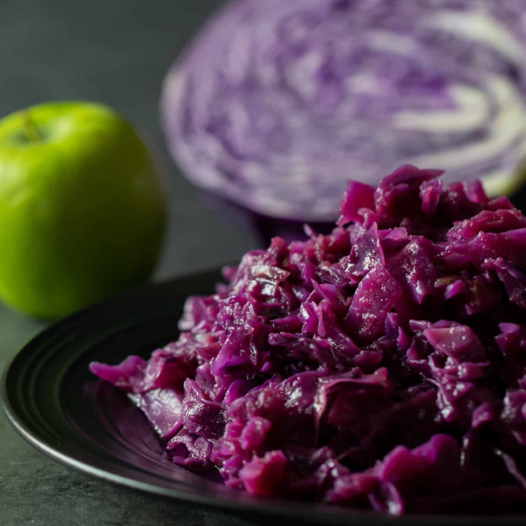 "Braised red cabbage on a black plate with a green apple and cabbage wedge"