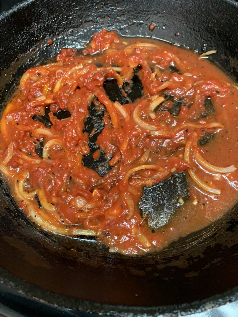 "A black frying pan with tomato paste, onions and thyme sauteeing"