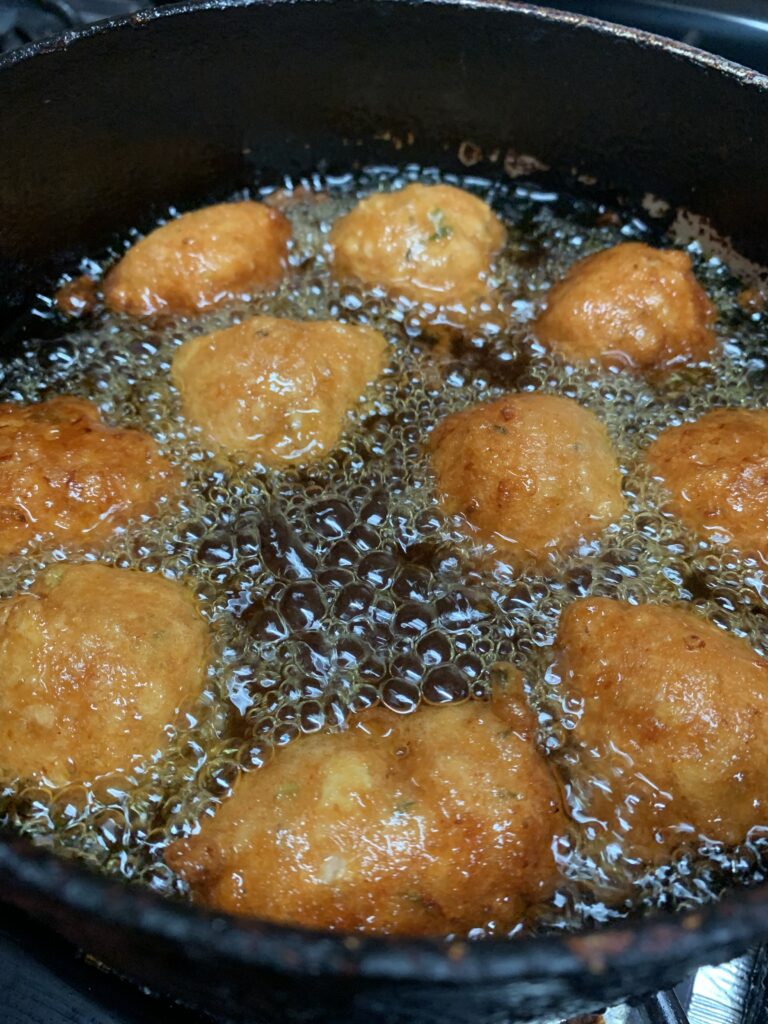 "Bahamian Conch Fritters frying in hot vegetable oil in a black pot"