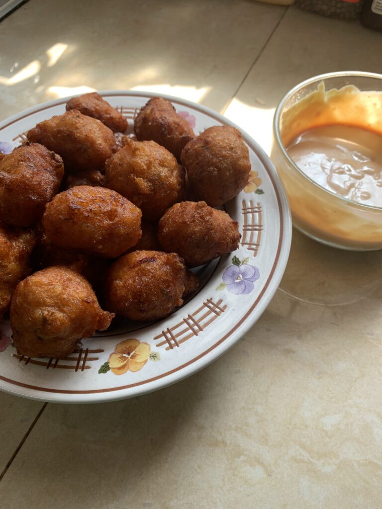 "Bahamian conch fritters with sauce in a white pattern plate on a cream tile background"