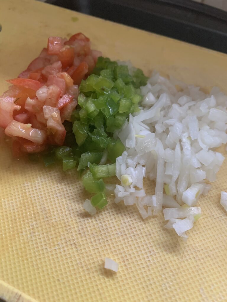 "Diced tomatoes, green bell peppers, onions on a yellow plastic cutting board"
