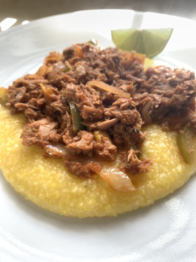 "A white plate with a wedge of lime, bahamian steamed tuna with yellow grits"