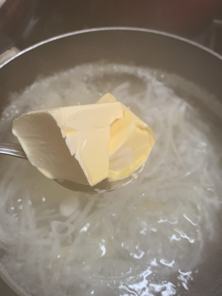 "adding butter to a pot of boiling water with onions"