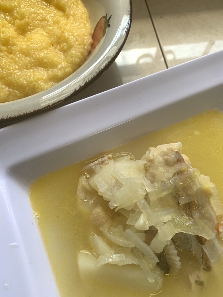 "Yellow grits with grouper fish, onion and potatoes in a broth in a white bowl"