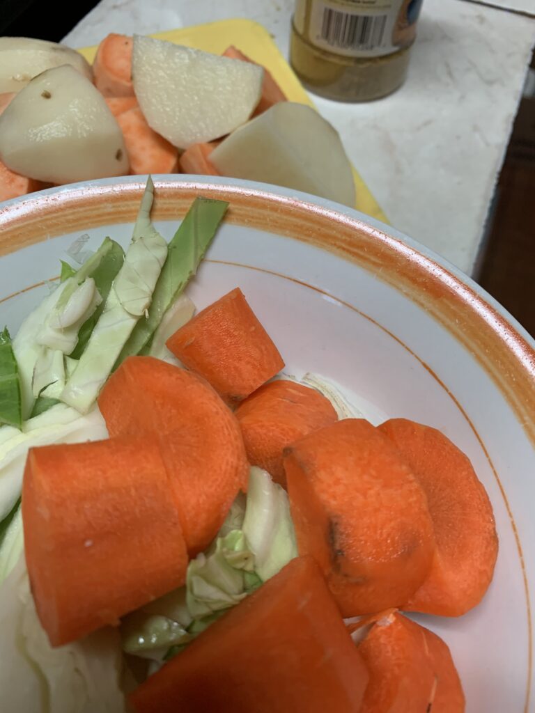 "Carrots, cabbage in a bowl, potatoes, and sweet potatoes on a cutting board"