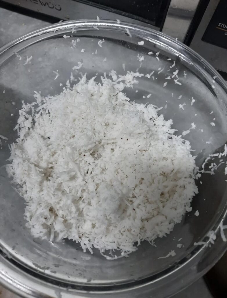 "Grated coconut in a clear bowl on a kitchen marble counter"