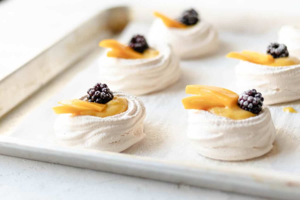 "Mini pavlova meringue ups topped with mango and blackberry fruits"