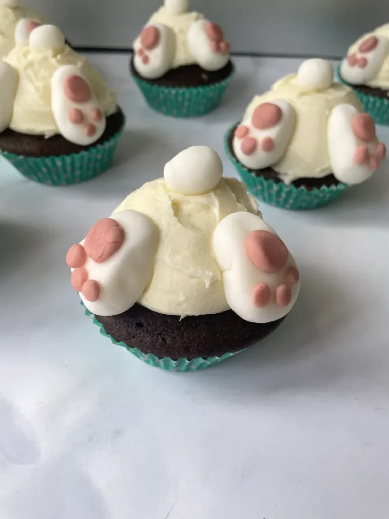 "Easter bunny cupcakes, pink and white feet, chocolate cupcake with white icing on white tile countertop