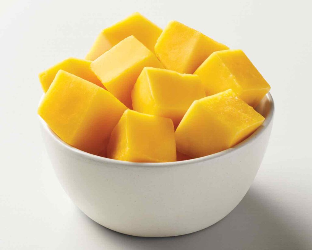 "A white bowl filled with diced mangoes on white background"
