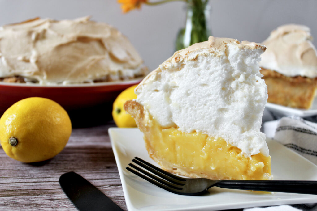 "Pie crust with half lemon custard with white meringue topping on a white plate with black fork"