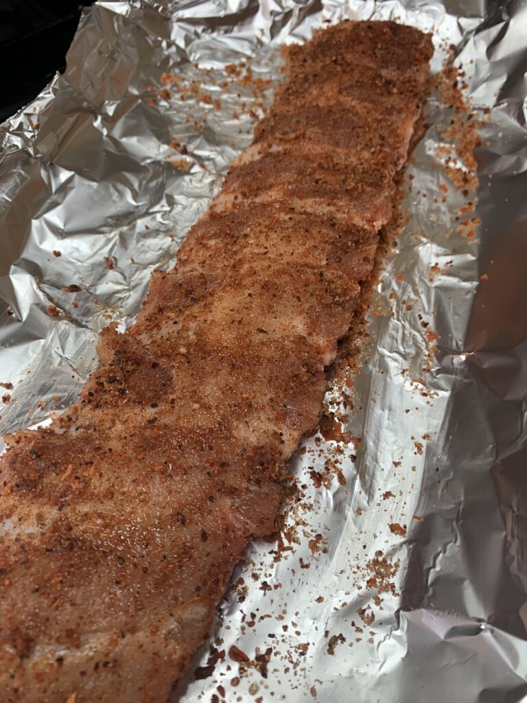 "A rack of ribs seasoned with a dry rub that included paprika in a foil wrap