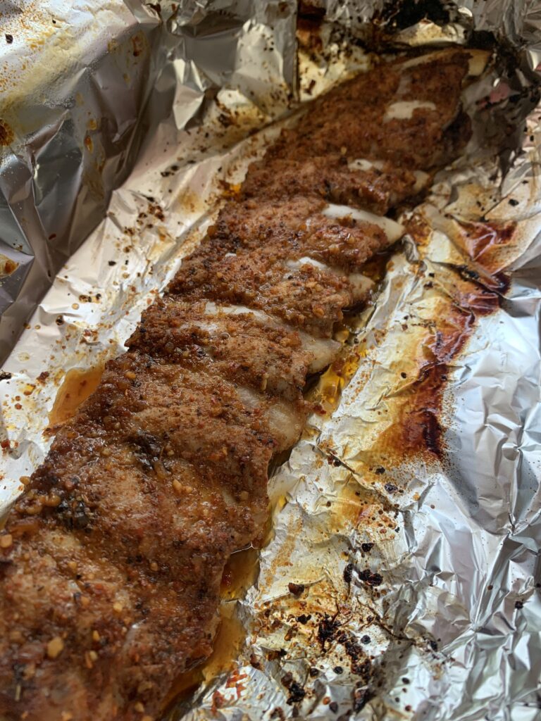"A rack of pork ribs already cooked in the oven coated in bbq sauce wrapped in foil paper