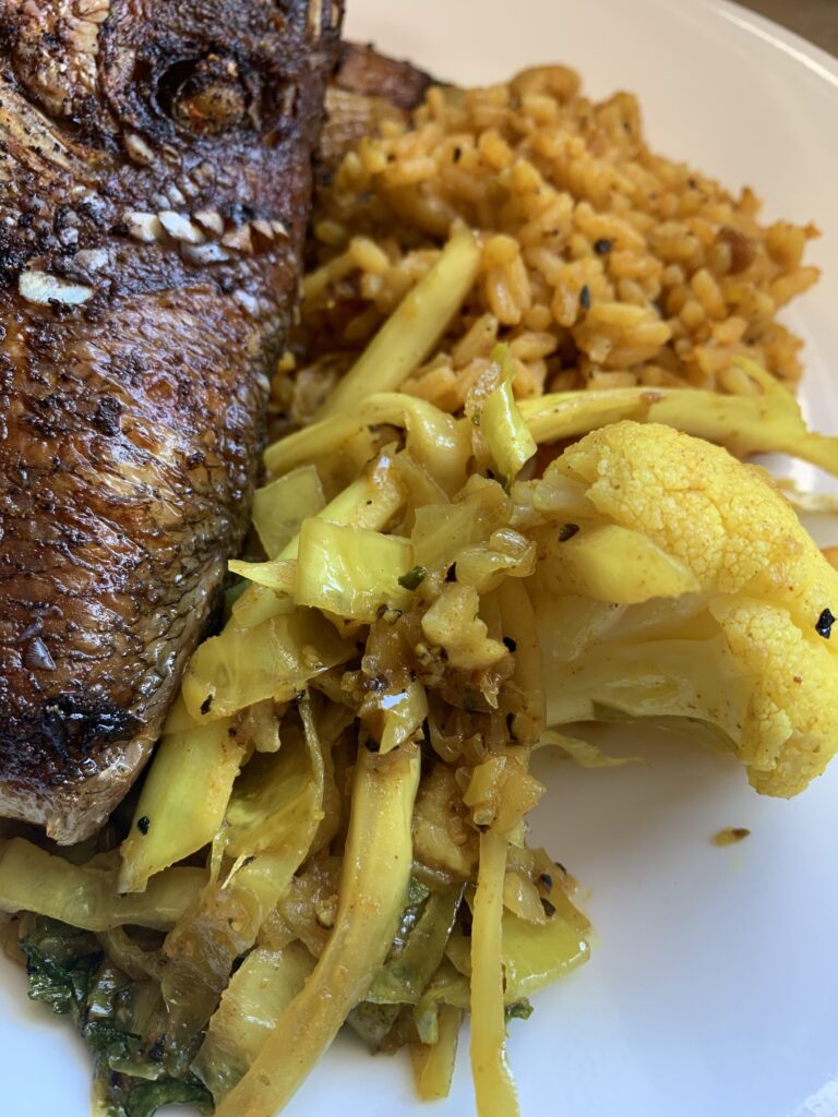 "sauteed cabbage, cauliflower on a plate with a fried piece of fish with brown rice"