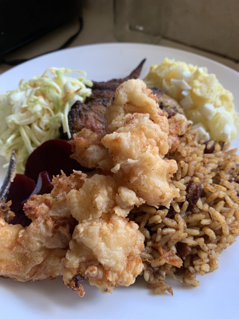 "A white plate filled with cooked food. Potato Salad, Coleslaw, Rice and Cracked Conch"
