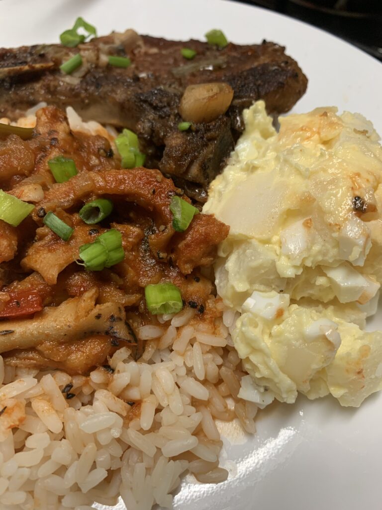 "A plate of cooked food with potato salad, white rice and steamed conch"