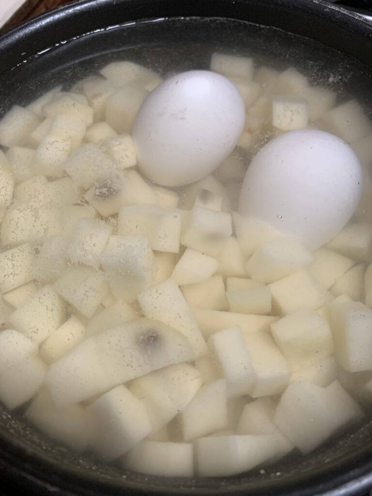 "A pot with diced potatoes, 2 eggs in its shell filled with water"