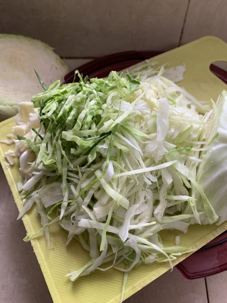 "shredded cabbage on a cutting board, with half a white cabbage in the background"