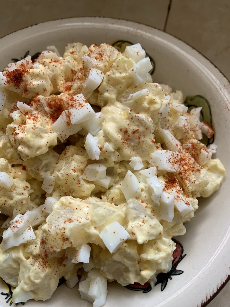 "Potato Salad in a bowl with topped with egg pieces and paprika"