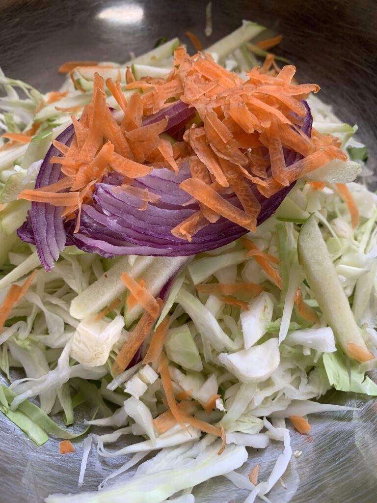 "shredded onion, papaya, carrots and green cabbage in a stainless steel bowl