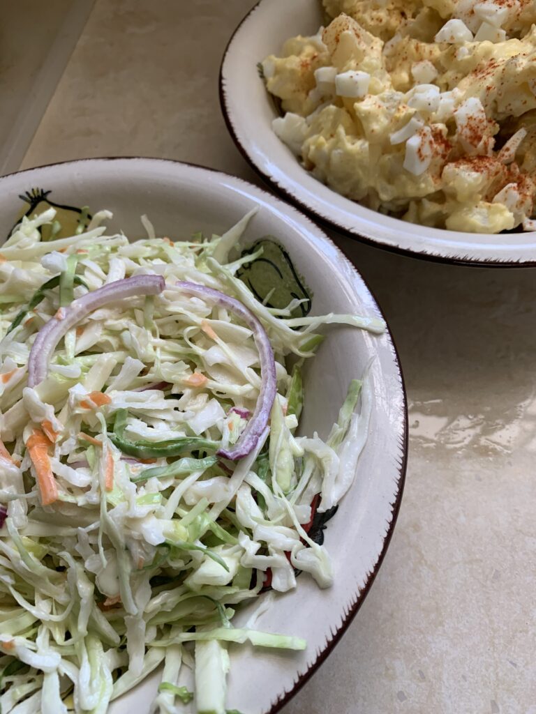 "a bowl of coleslaw and a bowl of potato salad on a tile counter top"