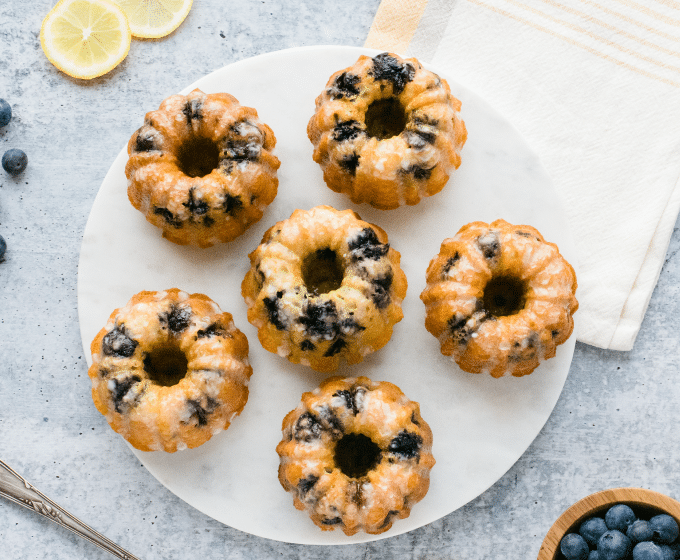 "Vanilla cake with blueberries and lemon on a white plate with lemon slices and blueberries on light blue background