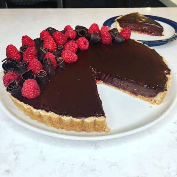 "Pie crust filled with chocolate ganache with raspberry decoration on a white plate"