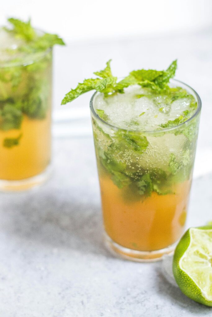 "A drink that is orange and clear with mint leaves on a tile countertop