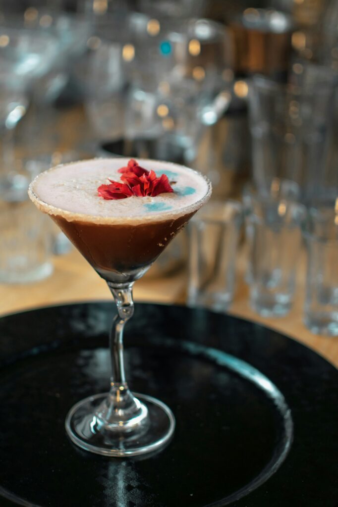 "A brown drink with a raspberry topping on a black plate with glasses in background"