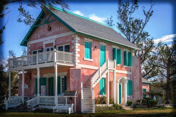 "A pink and green 2 story building with a porch and white trimming"