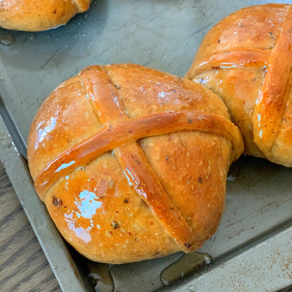 "Glossy hot cross buns ready to eat on a baking sheet"