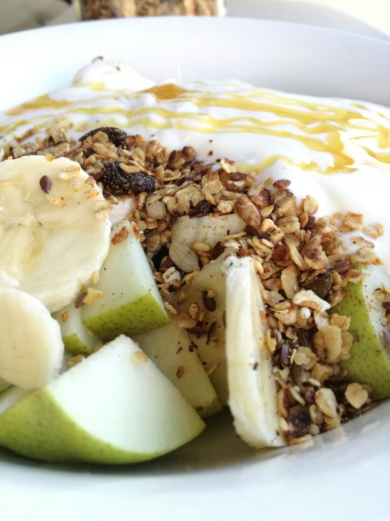 "Oats in a bowl with apples, banana drizzled with honey and topped with granola in a white bowl"
