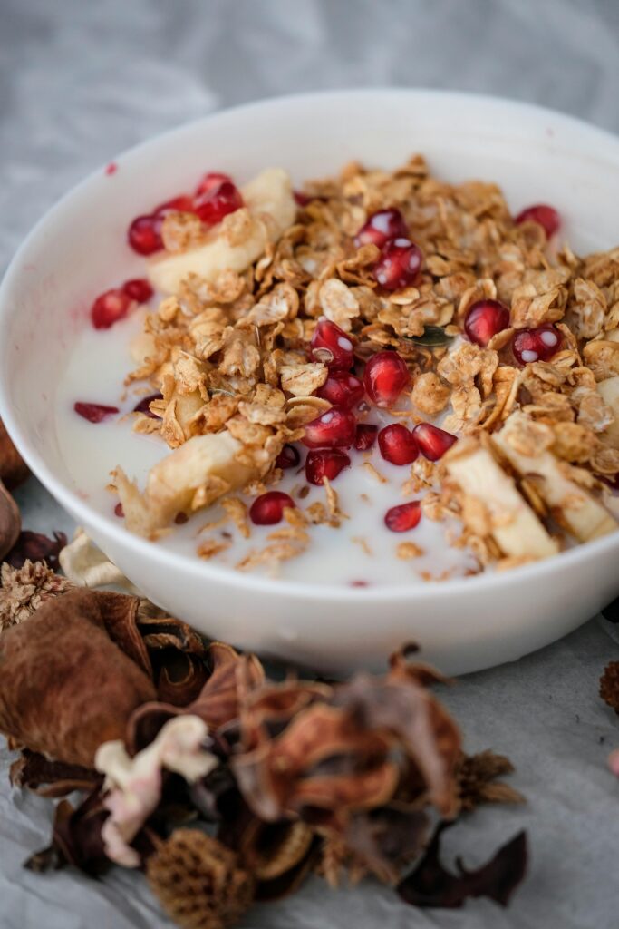 "Cooked oatmeal with granola, fruit and nuts o a tile background wiht cinnamon sticks and flower in the background"