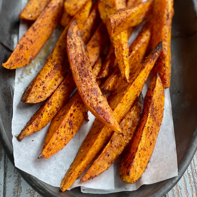 "Sweet potato wedges with seasoning on a white paper on a table"