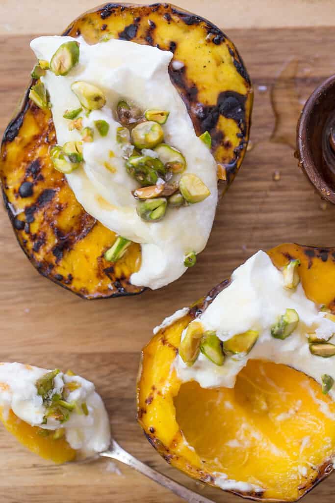 "grilled mango halves, topped with cream and pistachio nuts on a cutting board"
