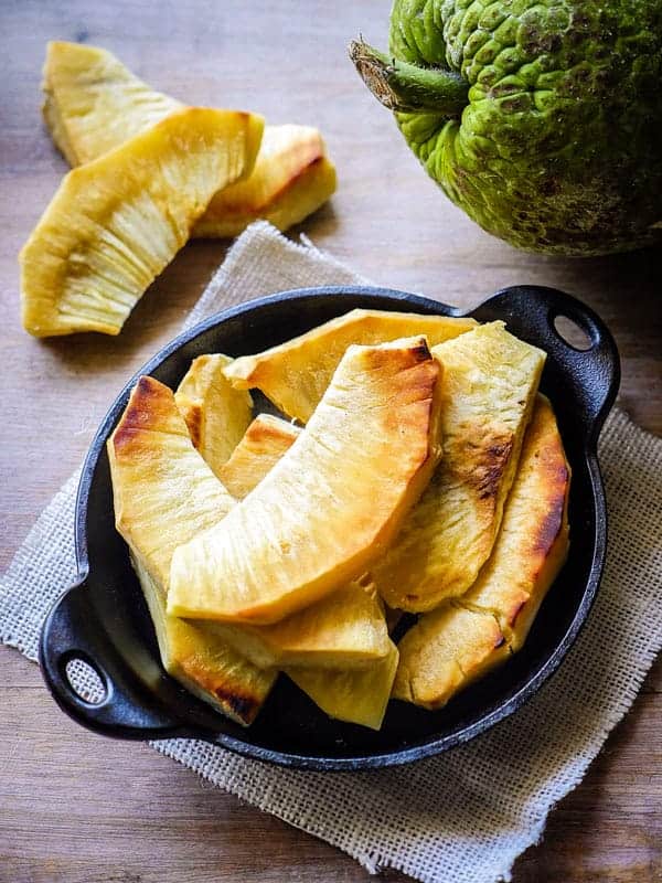 "Grilled breadfruit with a breadfruit in the background on a cutting board on a white napkin