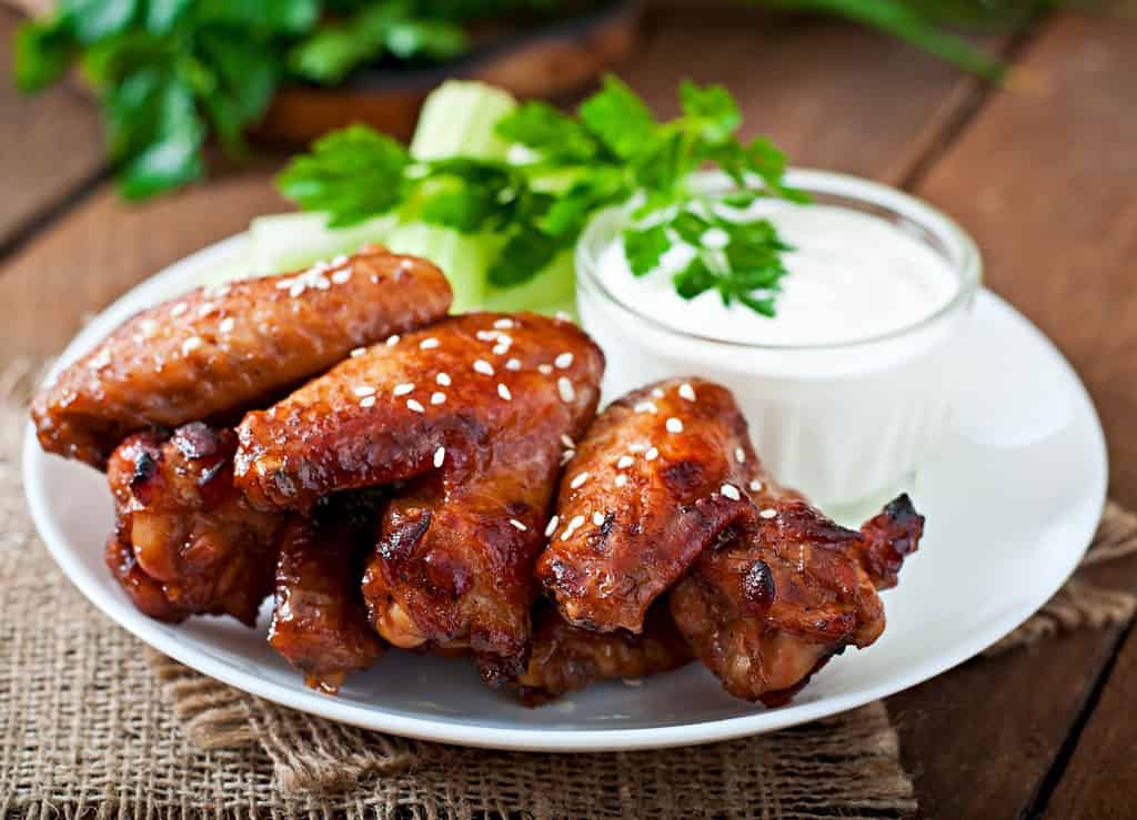 Glazed chicken wings with a dipping sauce on a white plate