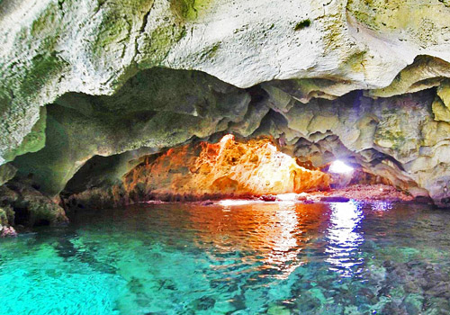 "a cave with gorgeous blue water with the setting sun in background"