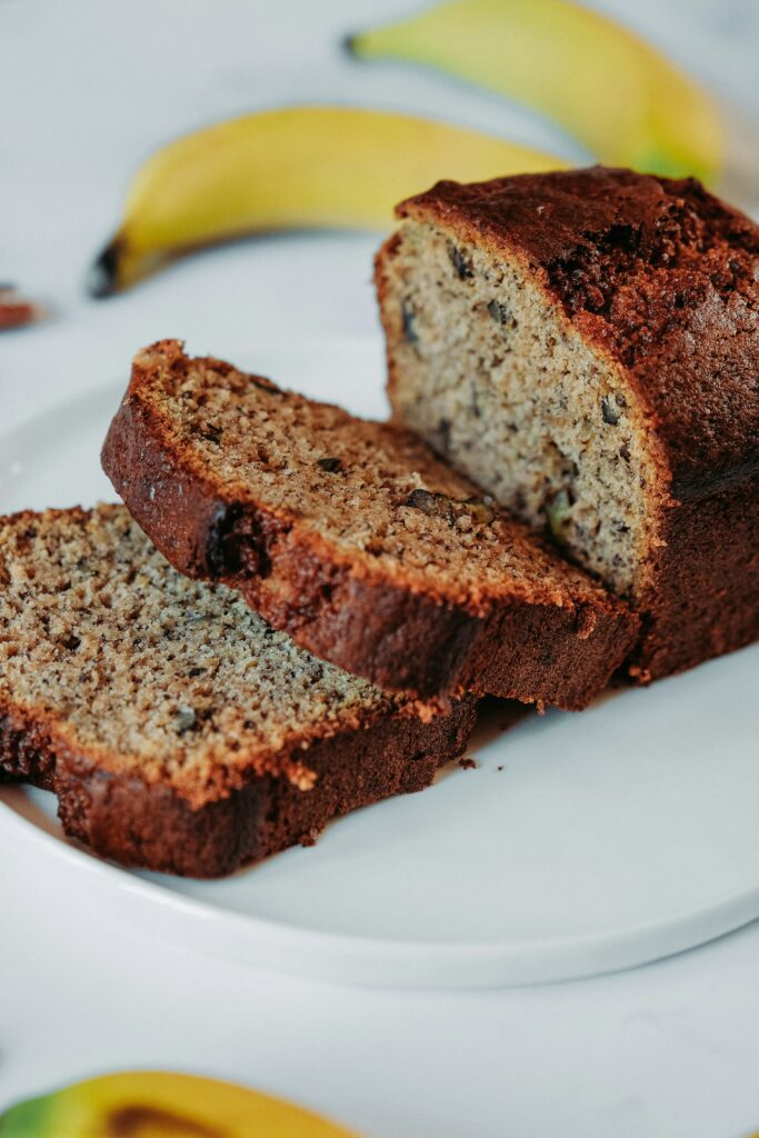 "Homemade banana bread sliced on a cutting board with bananas in the background"