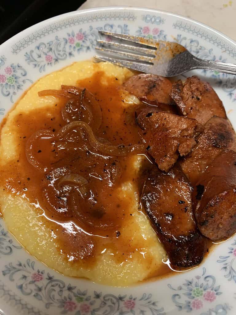 Yellow grits with fried sausage in a tomato paste gravy
