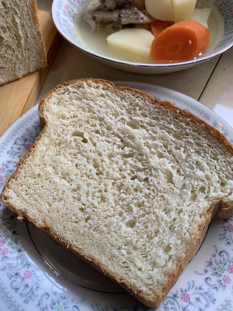 A slice of coconut bread on a white plate with flowers served with chicken in broth