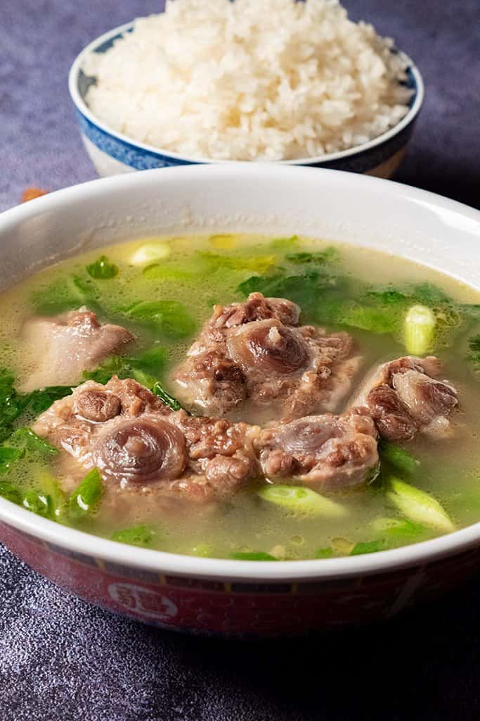 meat in a broth with greens in a bowl with white rice on the table